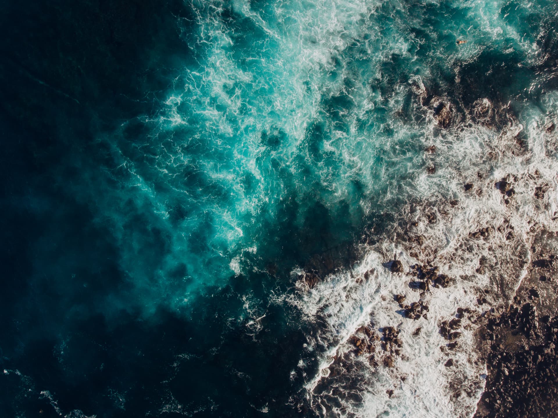 Aerial view of white water moving across deep blue-green ocean