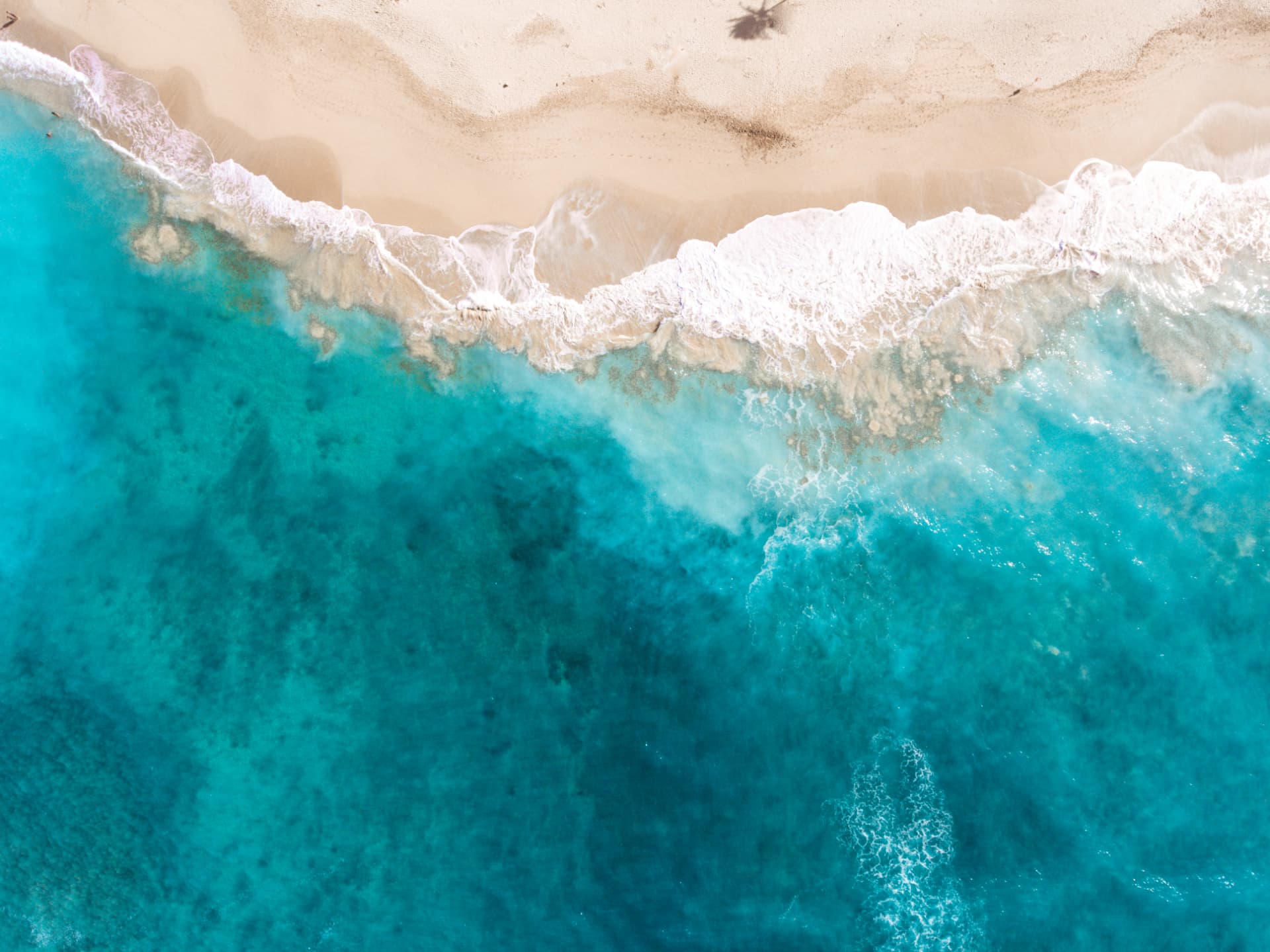 Aerial view of clear turquoise water washing onto pale sand
