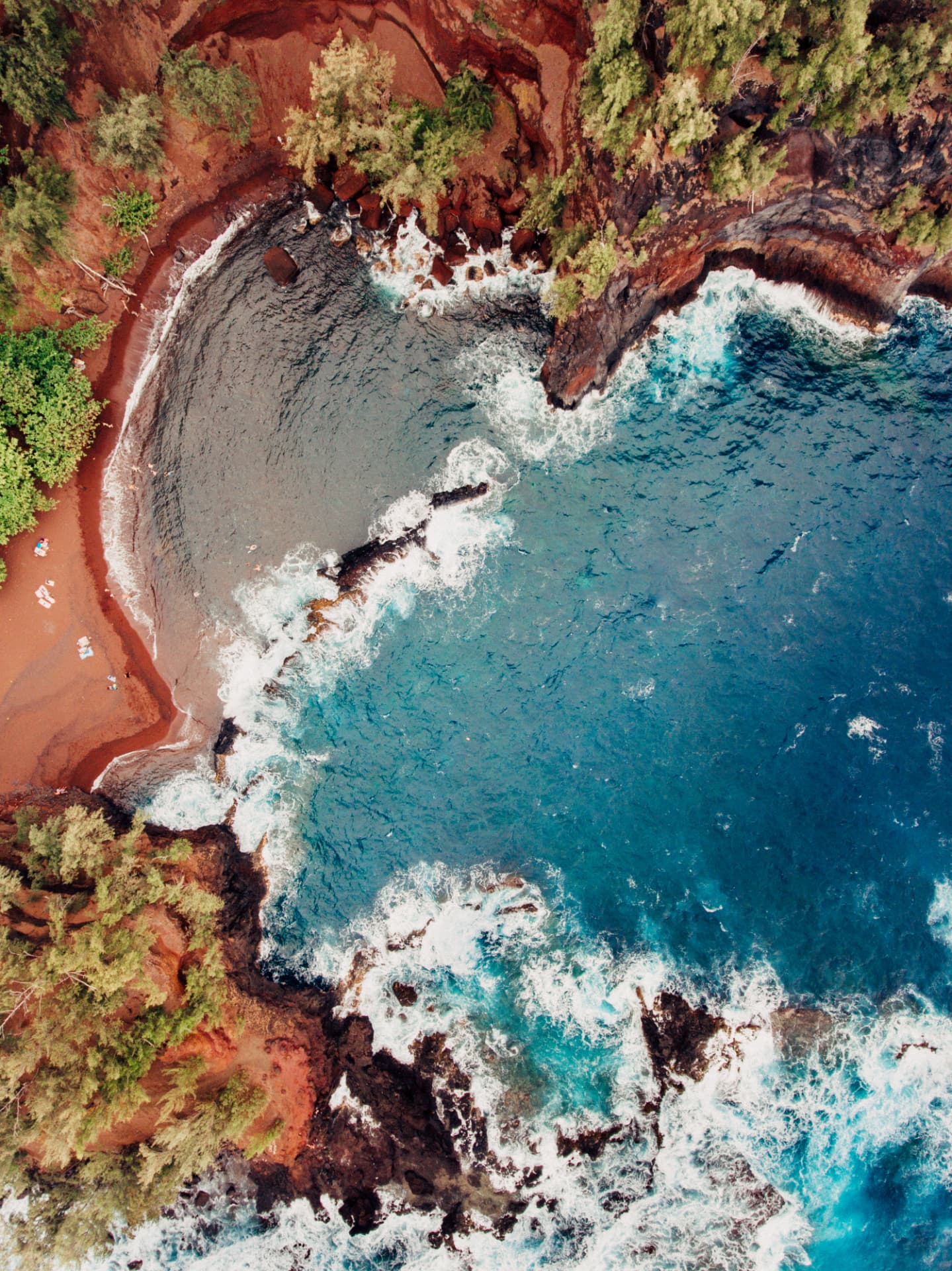 Aerial view of a red sand cove framed by dark rock and green trees